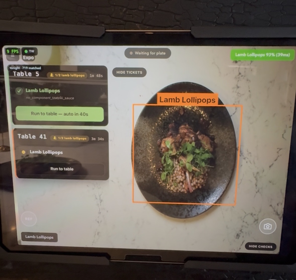 AyeQ matching a Lamb Lollipops plate to its Table 5 ticket — including the 'no tzatziki' modifier — and clearing it to run to the table